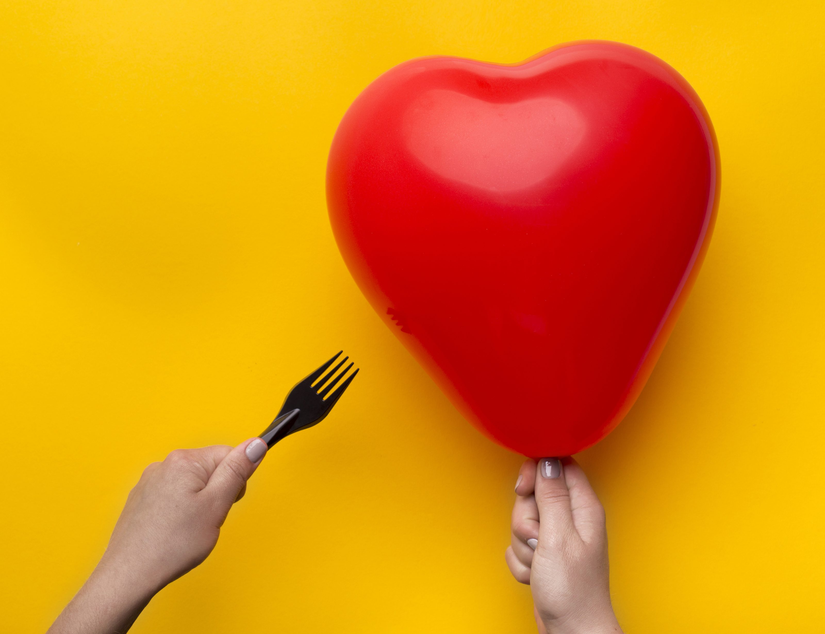 Woman holding red heart balloon and pinned with scissors over yellow